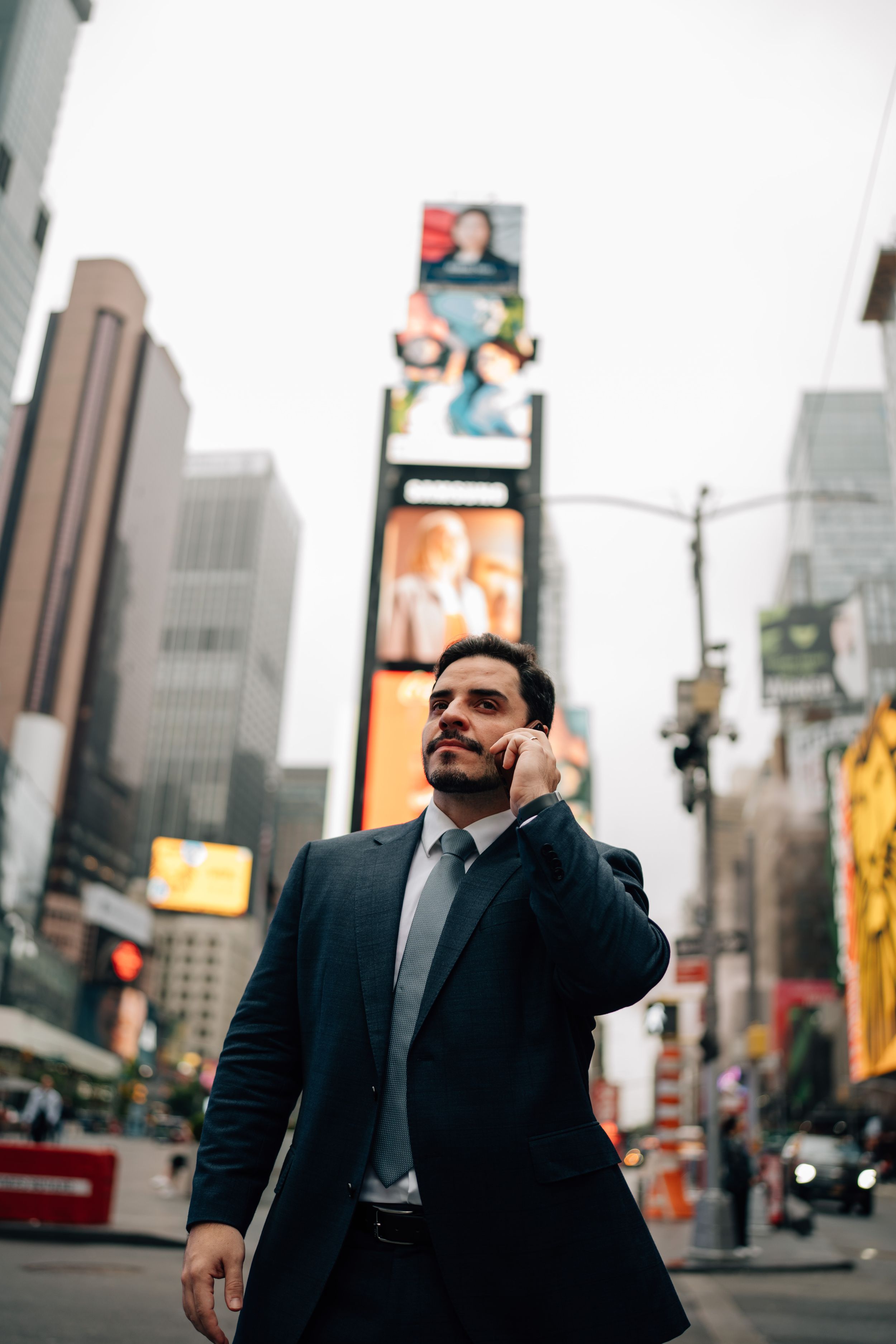 Businessman in suit talking on phone in Times Square, NYC, with illuminated billboards and skyscrapers in background.