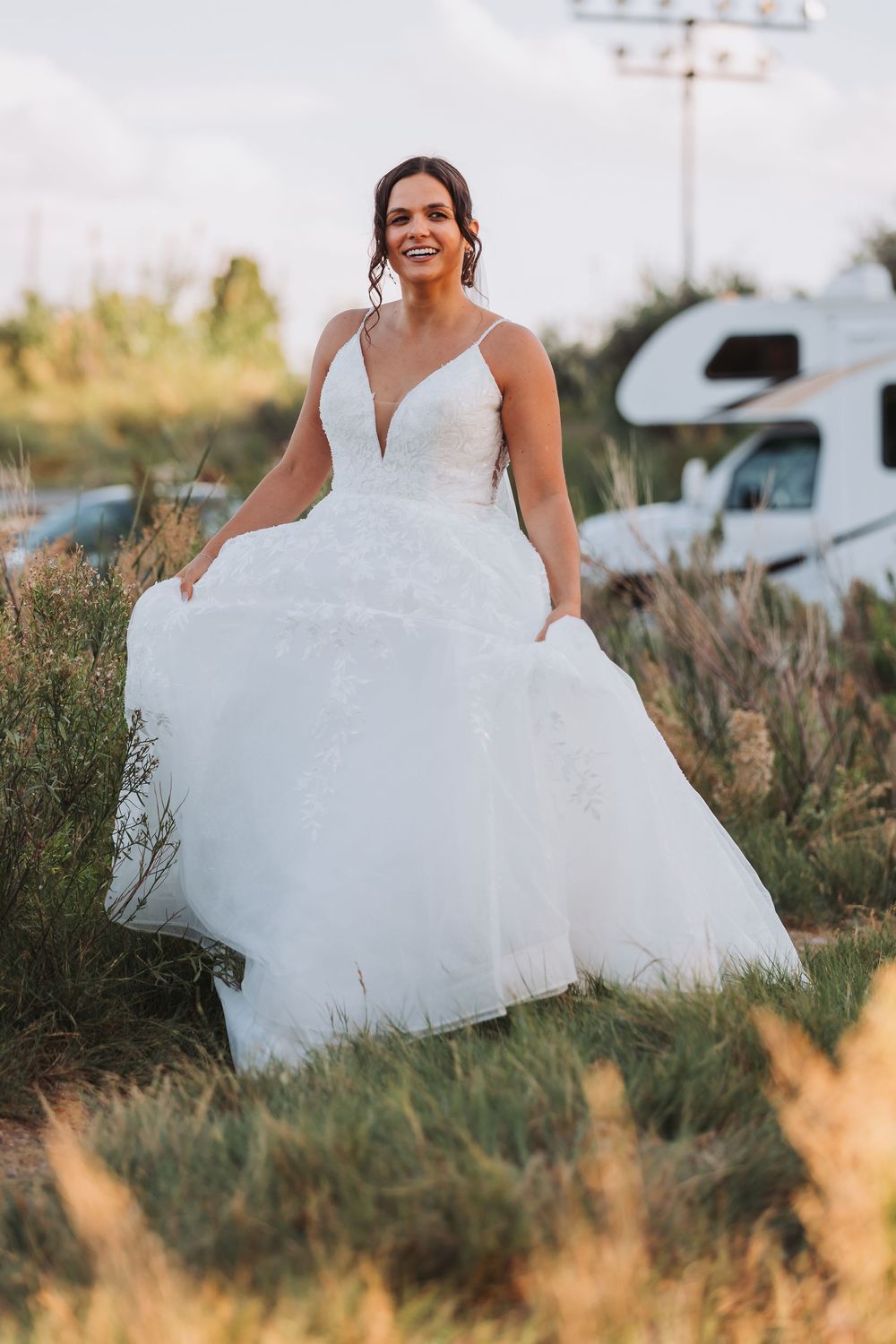 A bride in a flowing white ball gown twirls joyfully in a golden field during sunset.