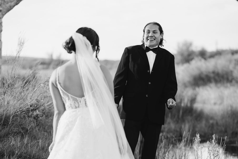 Black and white wedding photo of couple walking together in a field with bride's veil flowing in the breeze.