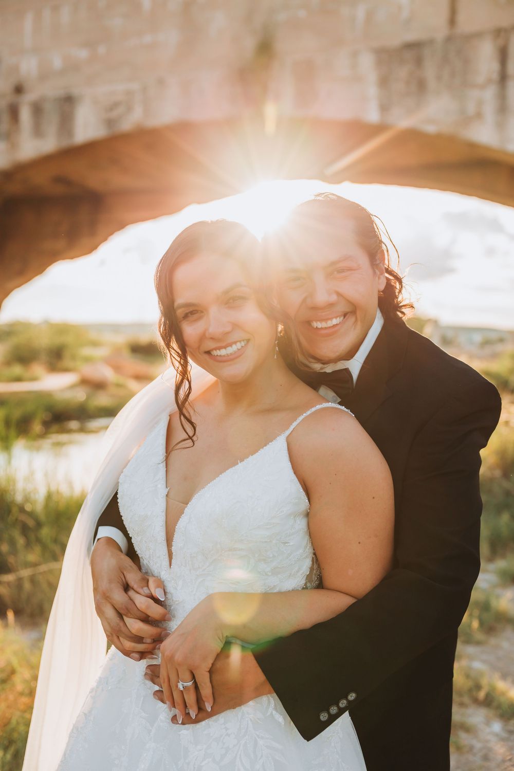 A romantic sunset photoshoot of a couple embracing outdoors with golden light creating a warm glow.