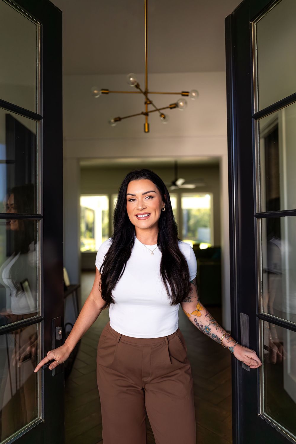 Professional photoshoot in modern office hallway featuring brown pants and white top outfit against dark windows.