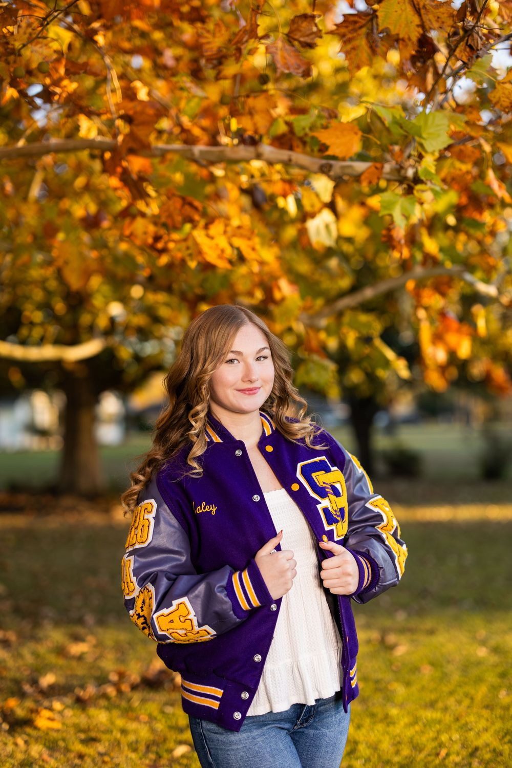 A letterman jacket photo session captured during golden hour with autumn trees in the background.