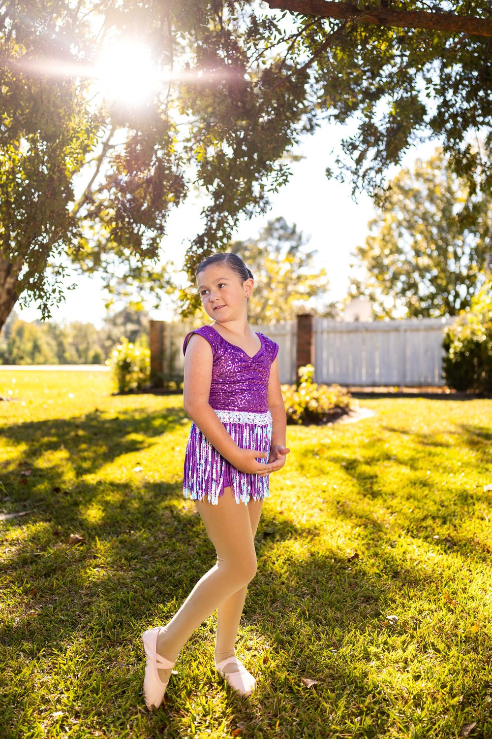 A sparkly purple dance outfit shimmers in the sunlit outdoor setting during a photoshoot.