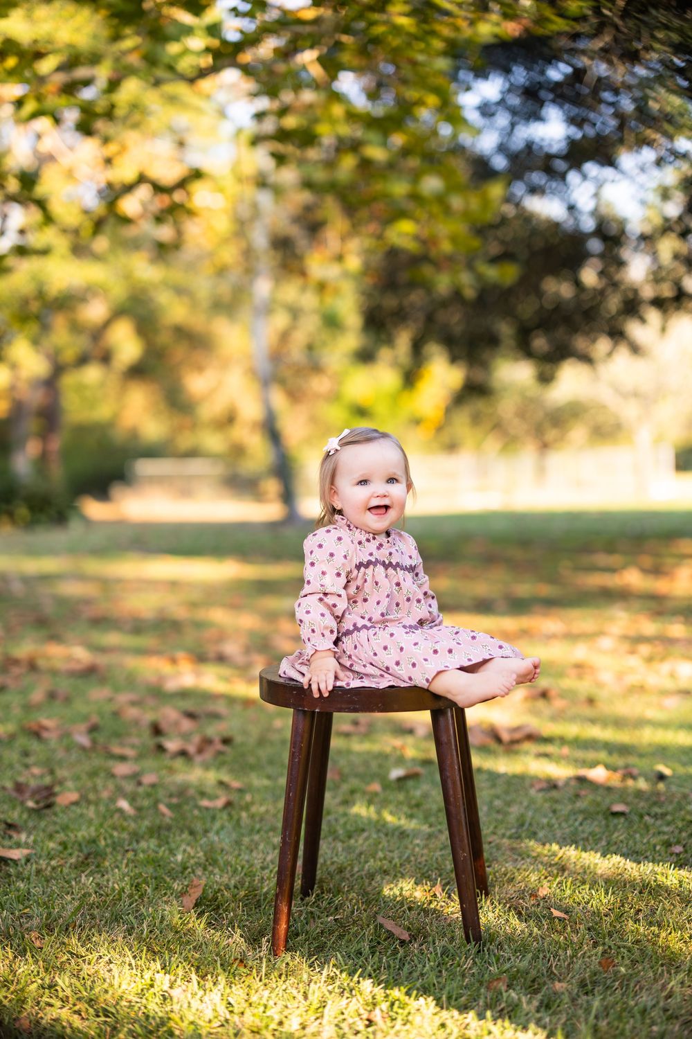 Child sitting on wooden stool in autumn park with golden sunlight filtering through trees.