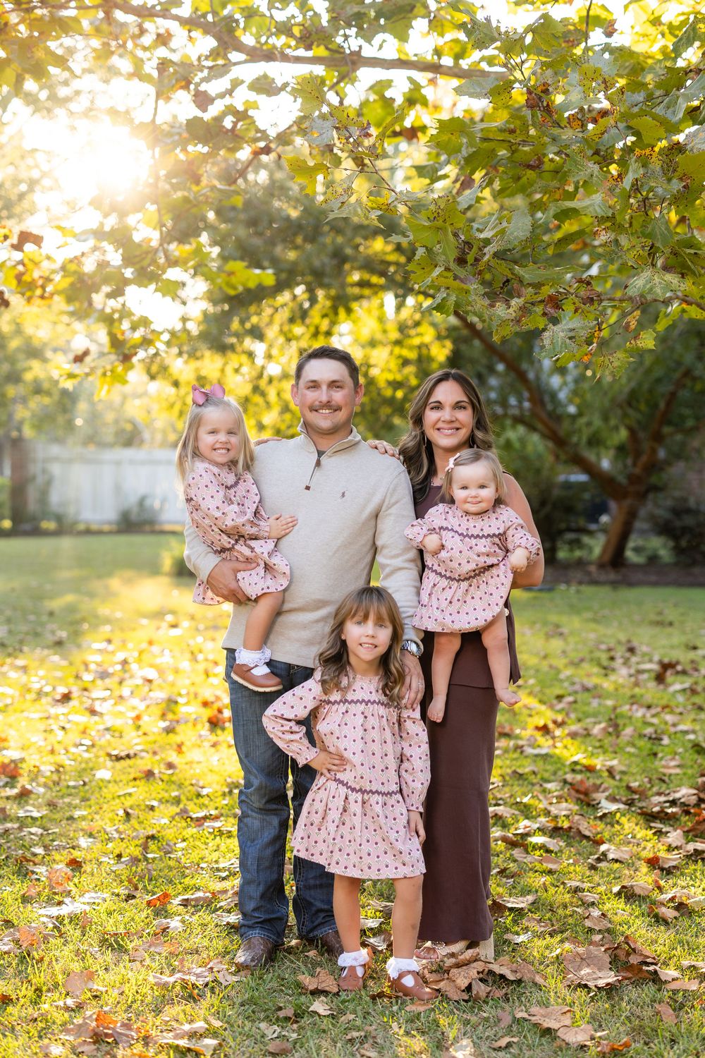 Family of four posing together on fallen autumn leaves in park setting.
