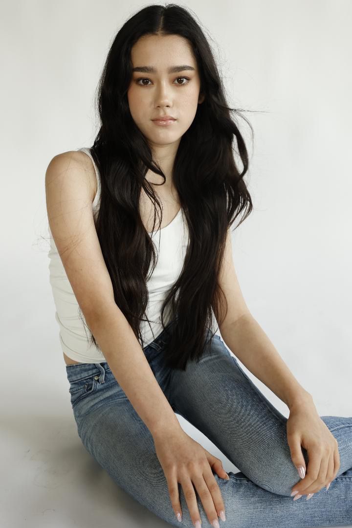 Person in casual attire sits on floor against white background in artistic portrait series.