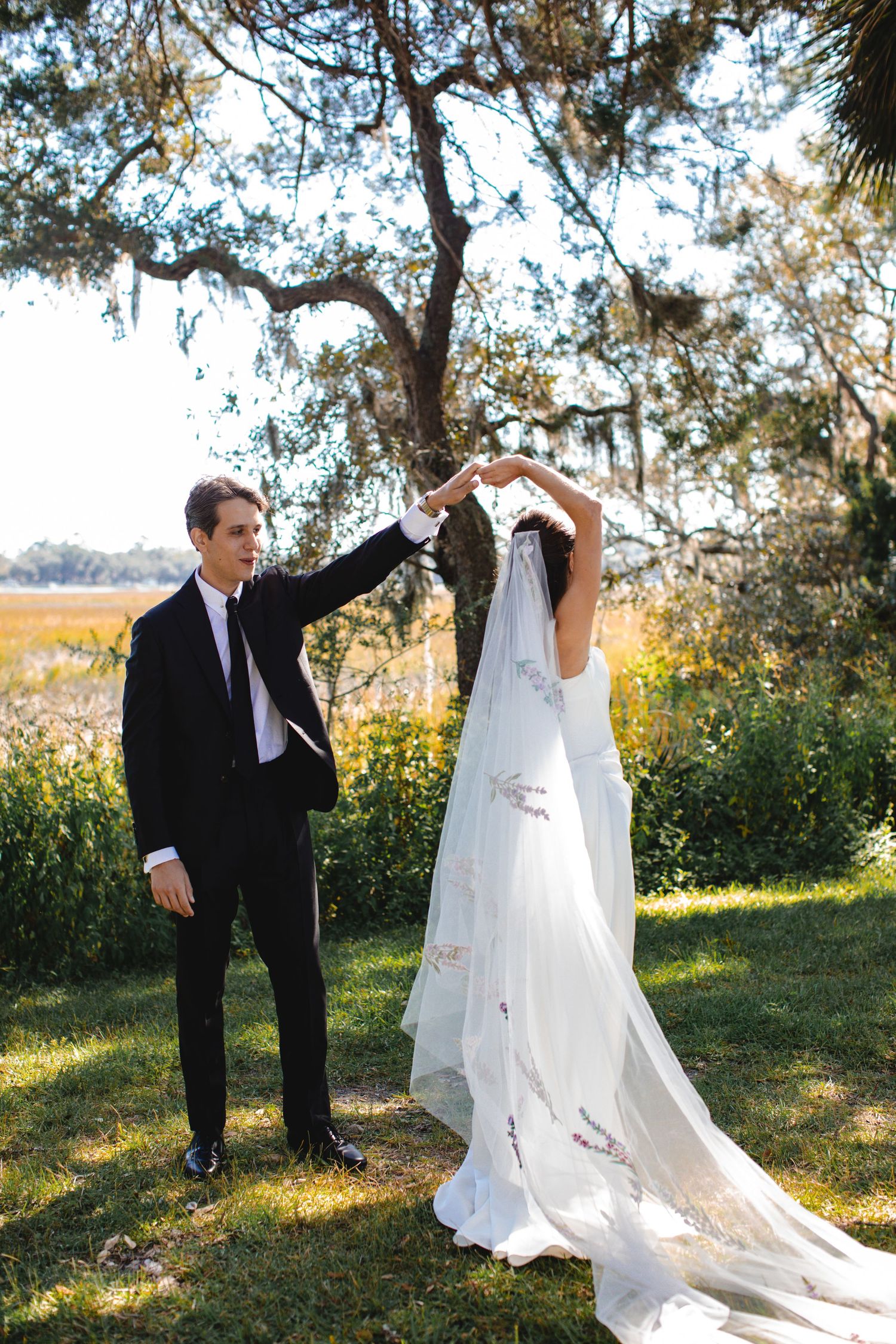 A romantic outdoor wedding photoshoot with flowing white veil and elegant poses in a sunlit garden setting.