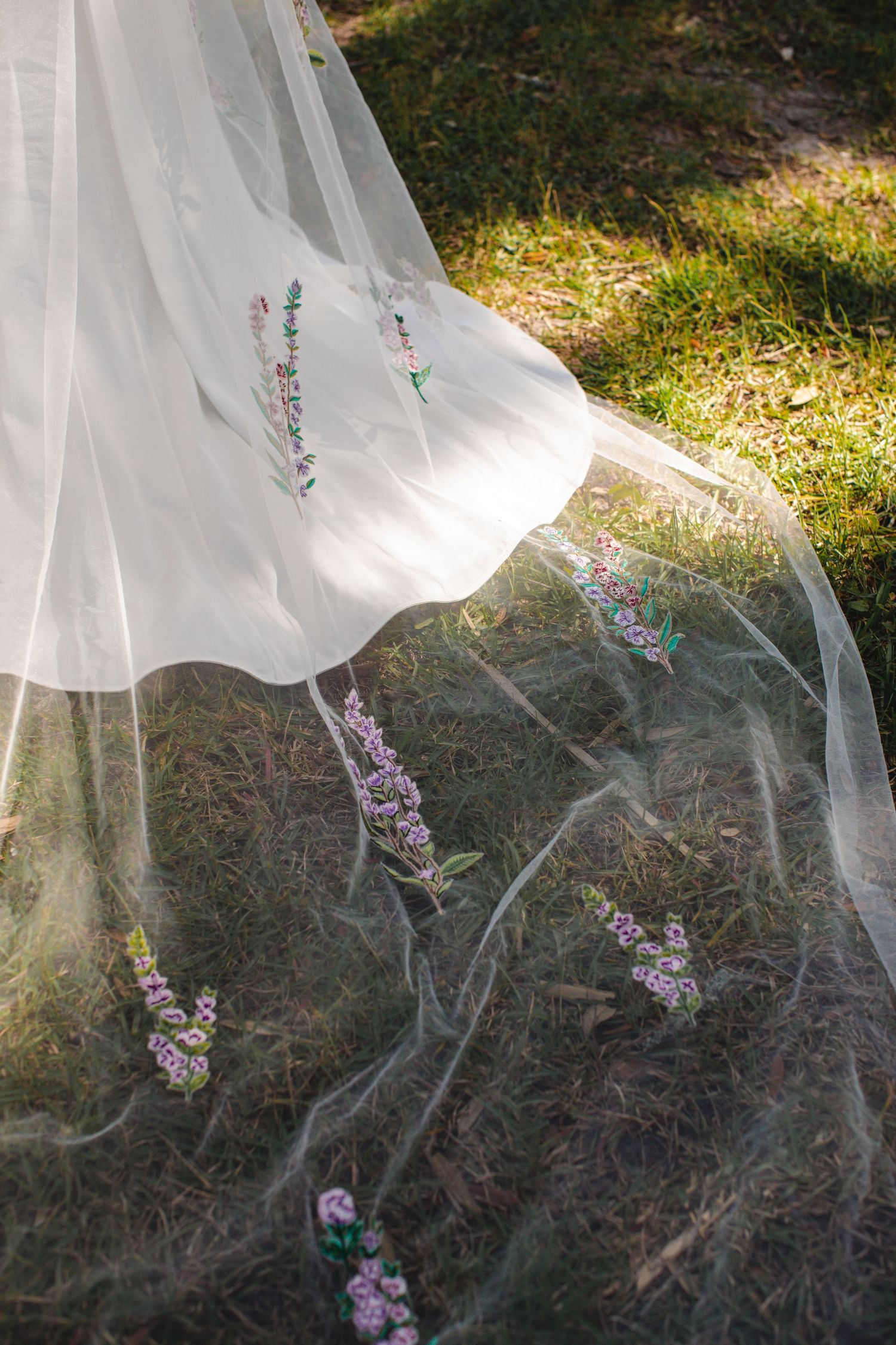 Delicate white wedding veil flowing in the breeze against purple wildflowers in natural outdoor lighting.