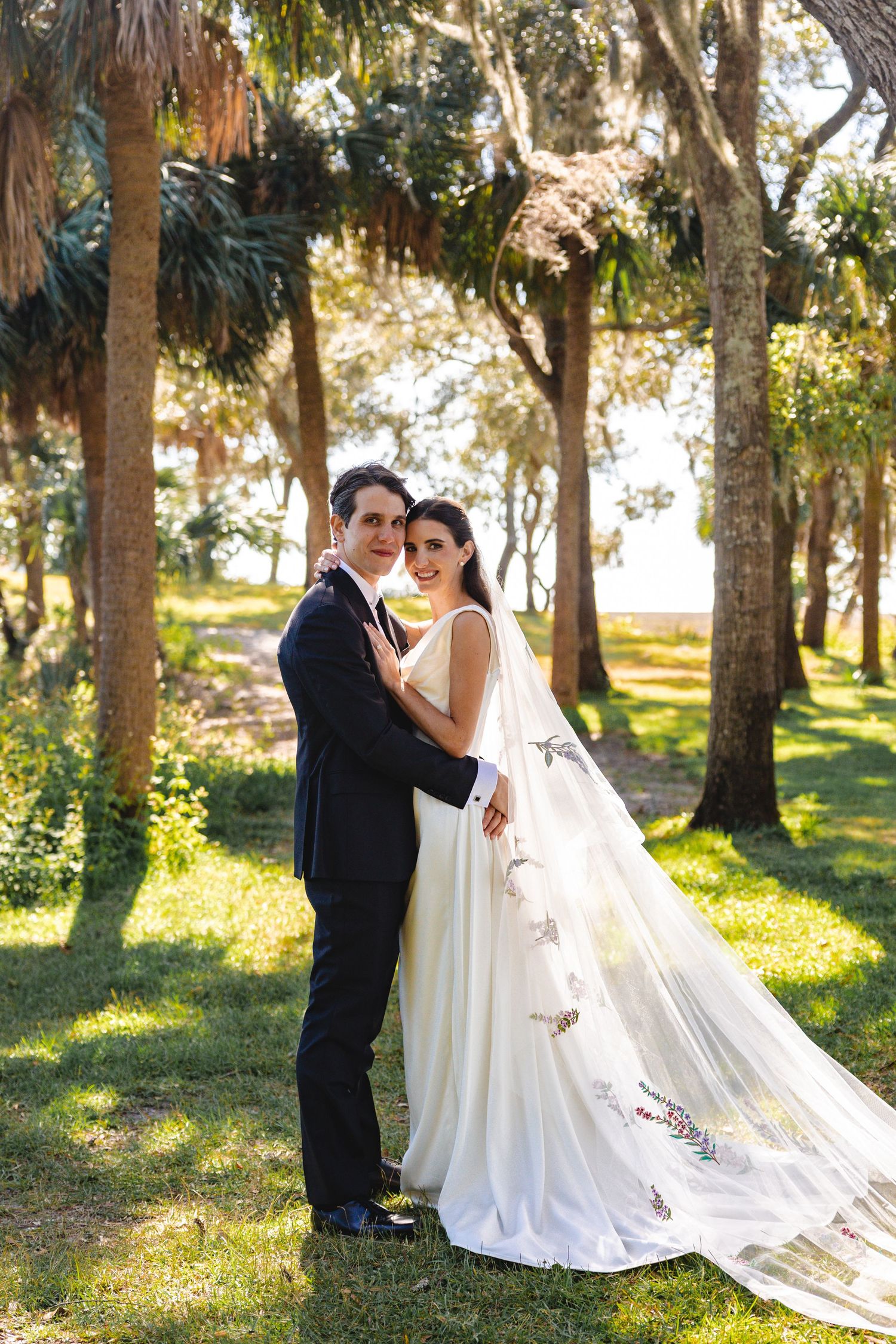 A romantic wedding couple shares intimate moments among sunlit trees in a dreamy outdoor setting.
