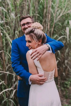 A couple shares an intimate embrace during their outdoor wedding ceremony surrounded by lush greenery and trees.