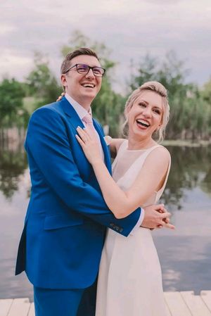 A couple in wedding attire laughs together during their outdoor photo session by a waterfront.