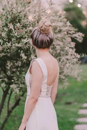 A bride in a sleeveless white gown poses in a garden with blooming cherry blossom trees in the background.