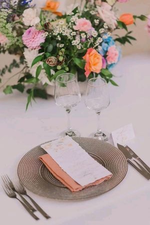 Elegant table setting with wine glasses and floral centerpiece featuring pink and orange roses on white tablecloth.