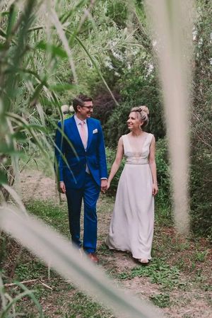 A couple in blue suit and pink dress share joyful moments while walking through a lush garden path.