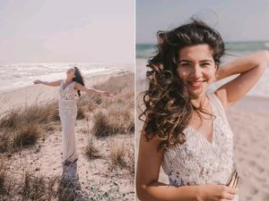 A woman in a white lace dress poses on a beach with windswept hair and natural coastal scenery.