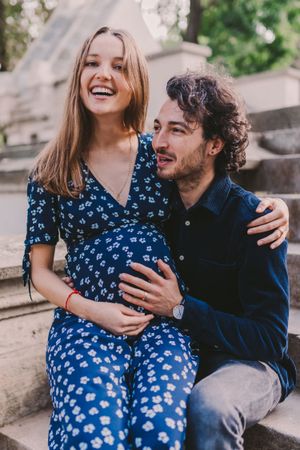 Intimate maternity photography session with couple sitting on stone steps outdoors.