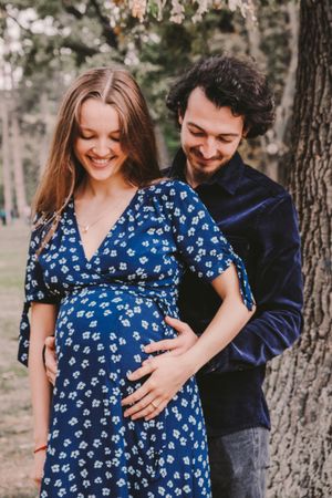 Romantic maternity photoshoot sequence in a forest setting with couple in blue floral dress.