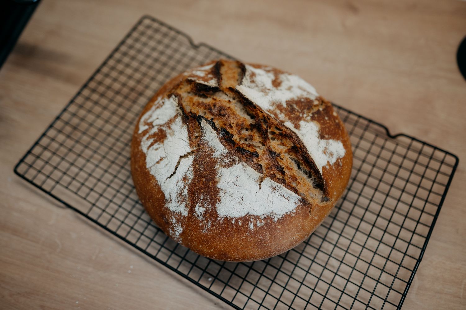 Freshly baked artisanal sourdough bread loaves cooling on wire racks with dusted flour and dark crust patterns.
