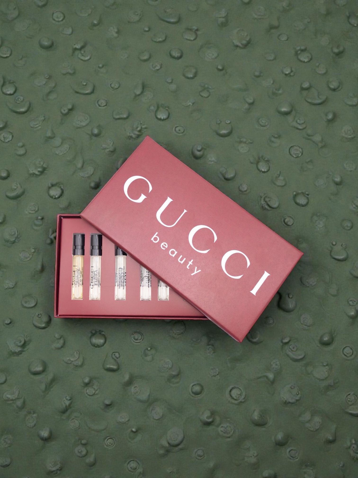 Multiple Gucci branded pink gift boxes arranged on a textured green background with water droplets.
