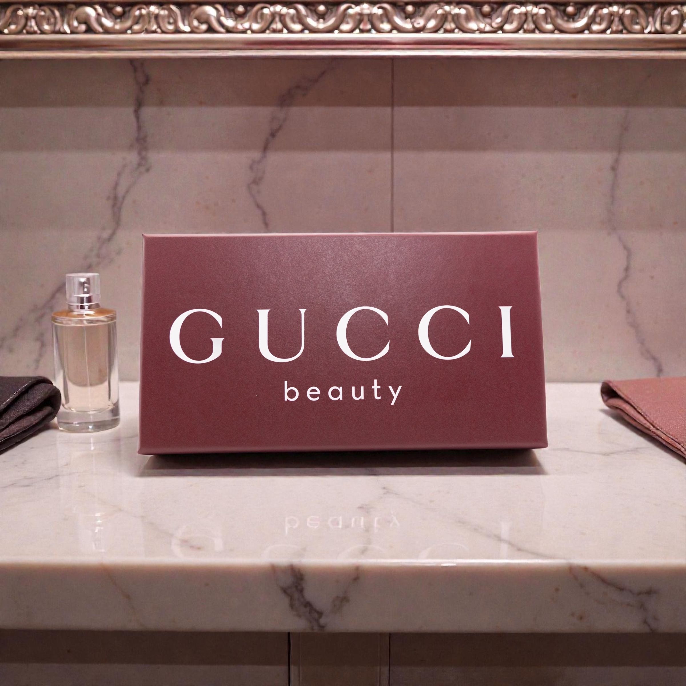 A Gucci Beauty logo sign displayed on a marble counter with a perfume bottle and accessories.