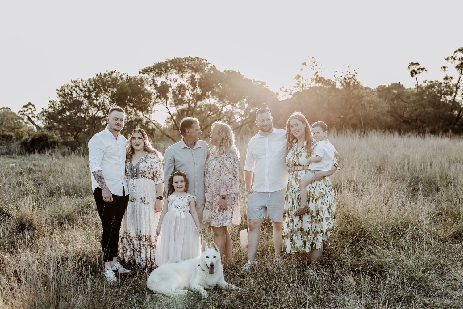 Large family group posing together in a sunlit meadow wearing coordinated outfits.