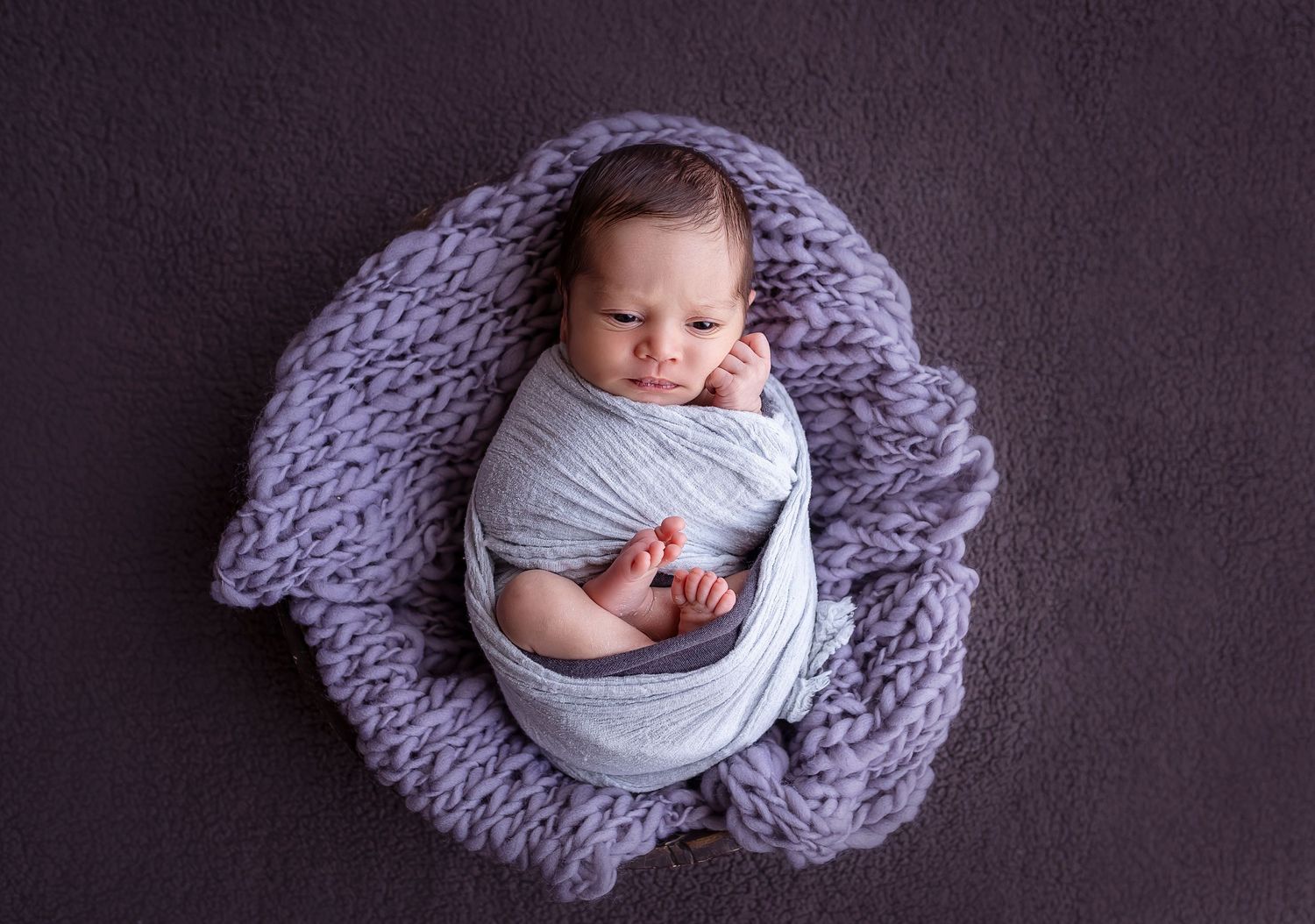 bebe envuelto en un wrap color gris acostado encima de un tejido dentro de un bowl de madera