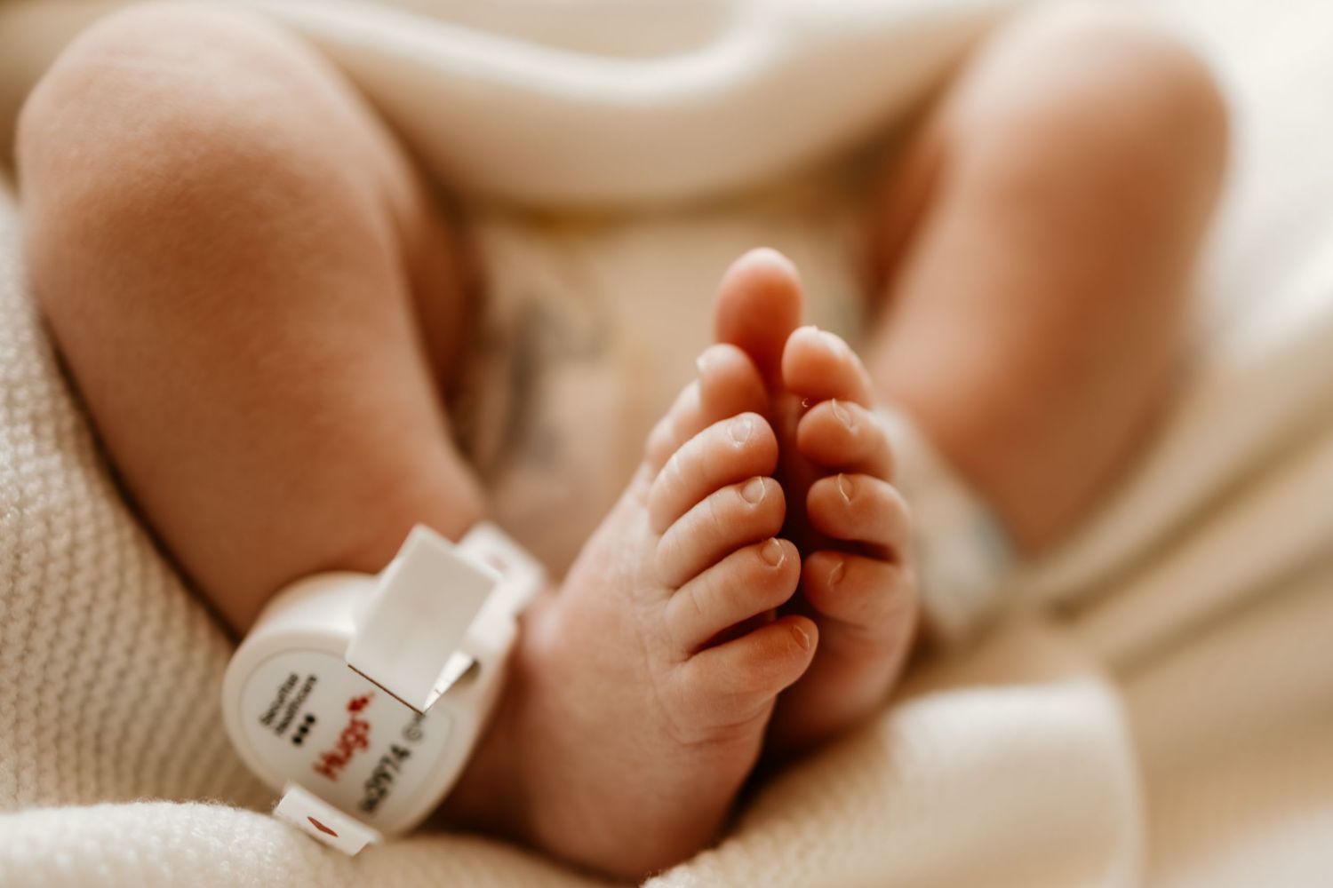 Close up of newborn baby's tiny feet with hospital identification bracelet.