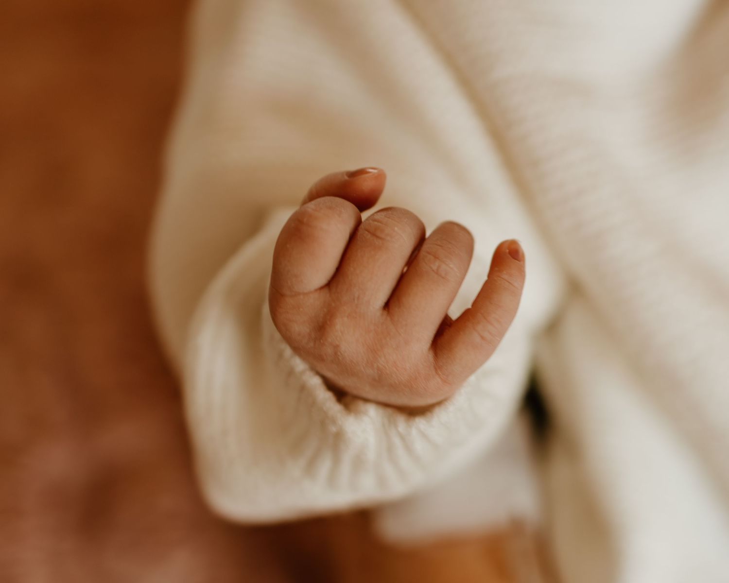 A tiny baby's hand reaches out from a white knitted sleeve.