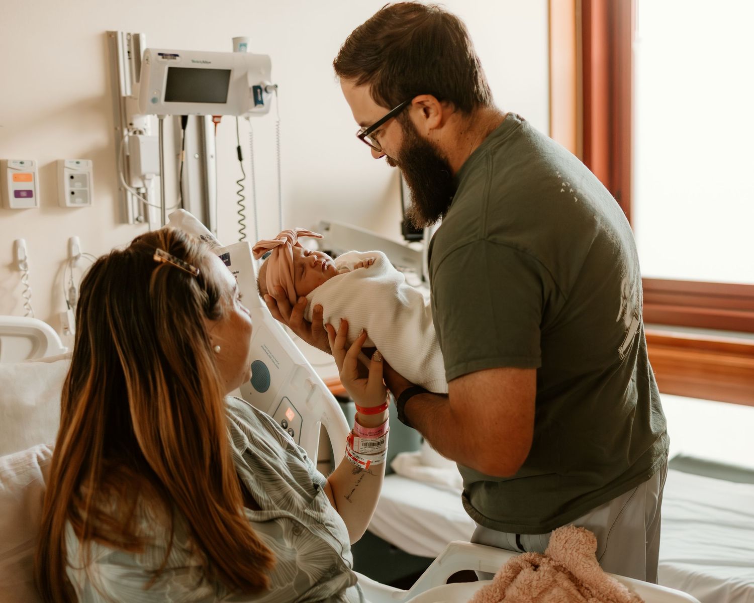 A tender moment in a hospital room as a newborn baby is cradled while medical equipment monitors in the background.