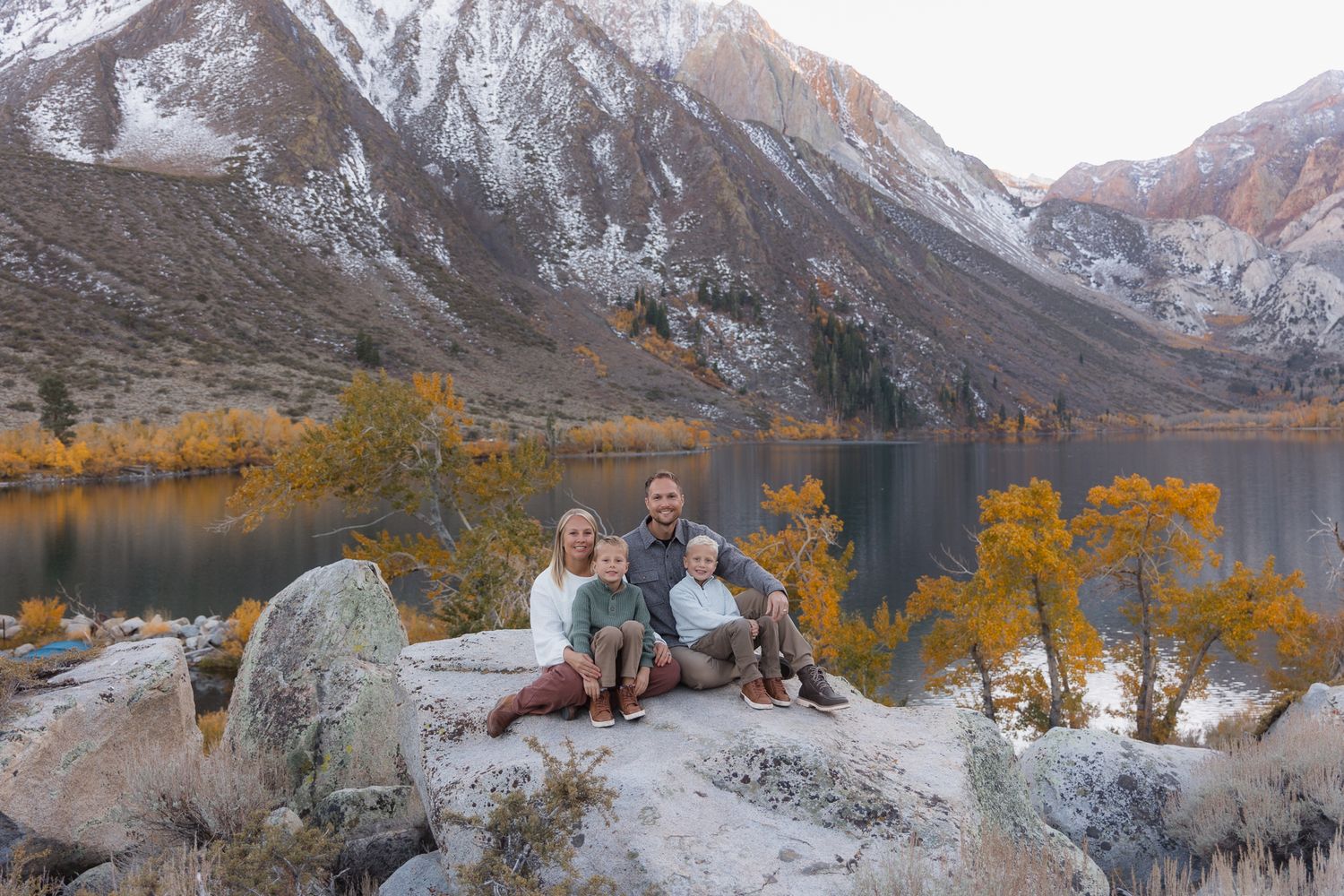 Group sits together on grassy field with majestic mountain range in background during golden hour.