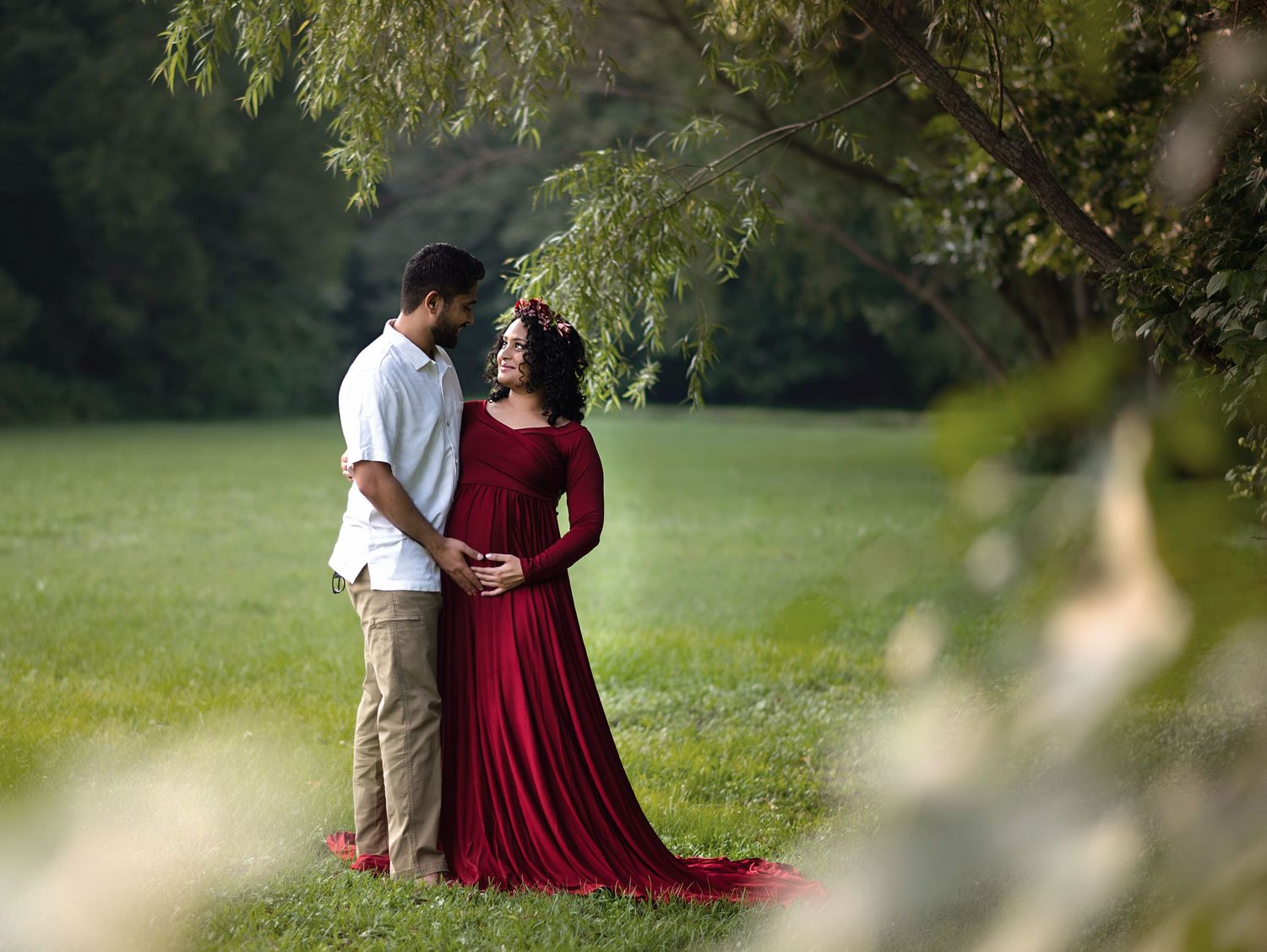 A couple in a grassy field, with the woman wearing a flowing red dress.
