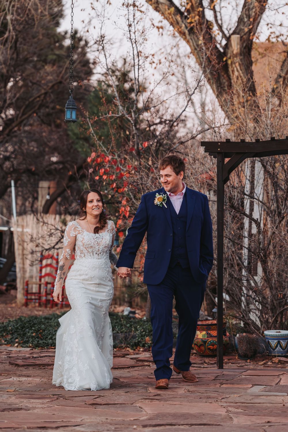 A couple walks together through a garden path during an autumn wedding photoshoot.