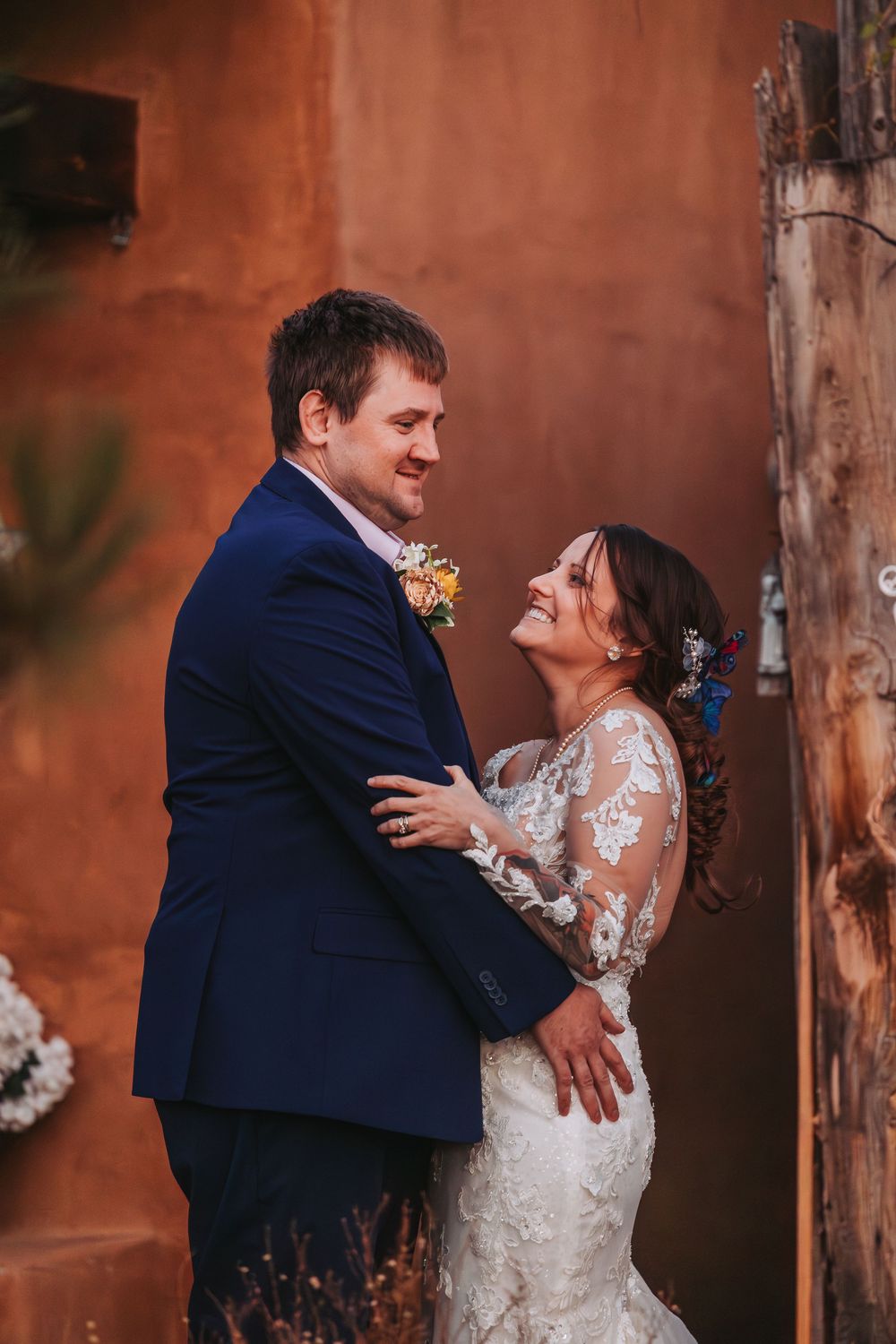 A bride and groom share an intimate moment together against a rustic terracotta wall at their wedding celebration.