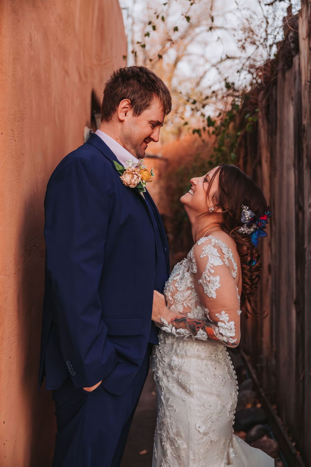A romantic wedding couple shares an intimate moment against a rustic wall at sunset.