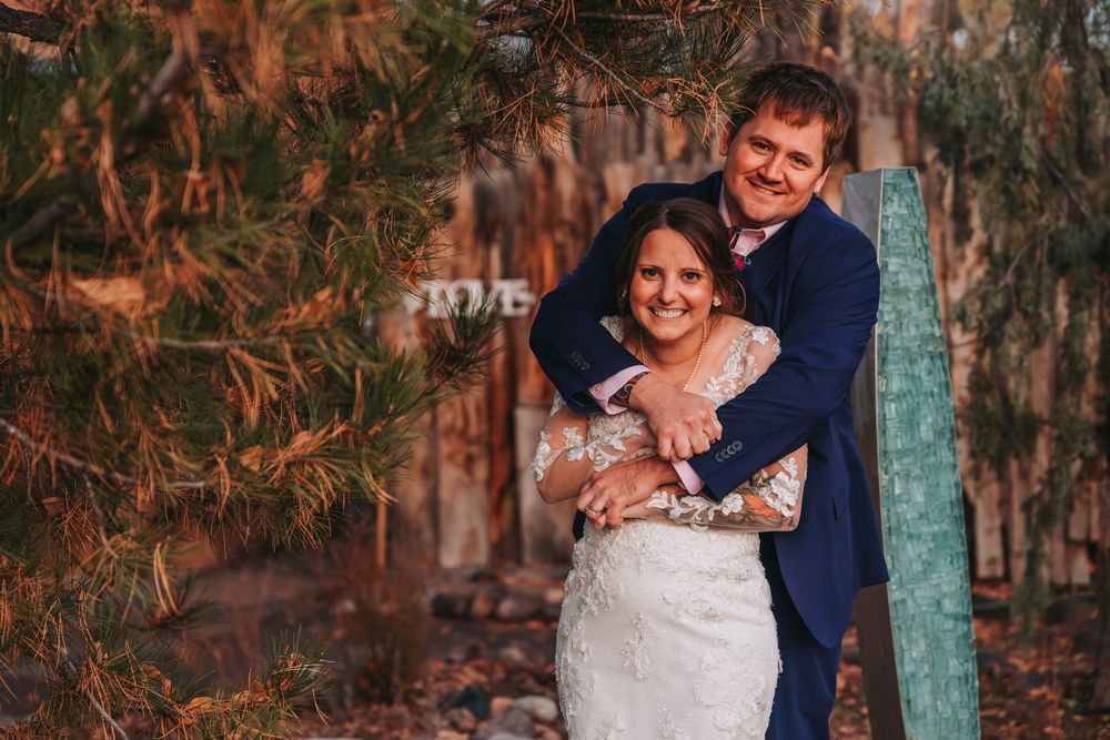 A couple shares a romantic moment in a garden setting with rustic wooden elements and natural lighting.