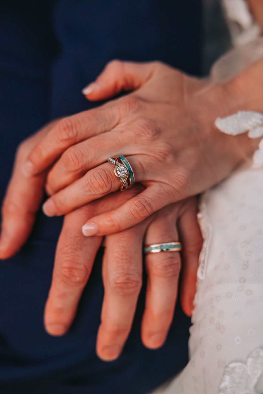 Close-up shots of hands wearing wedding rings against white lace and navy blue fabric backgrounds.