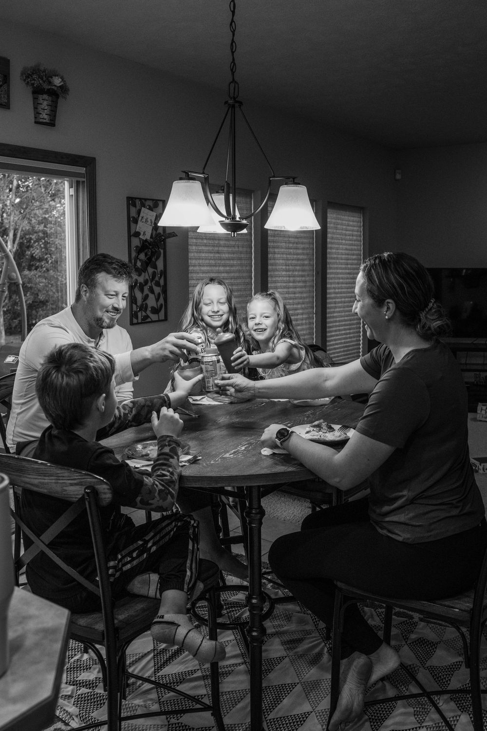 Black and white photo of people sharing dinner around a table in home setting.