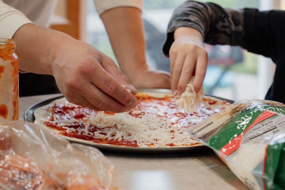 A collage showing hands decorating homemade pizzas with various toppings and ingredients on a wooden surface.