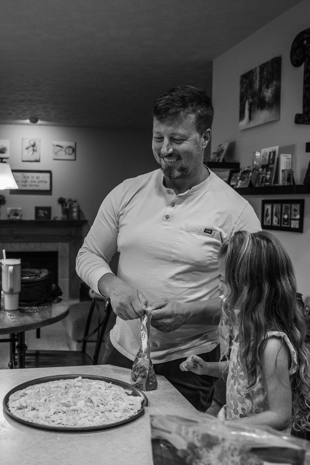 A black and white photo showing pizza preparation at a kitchen counter.