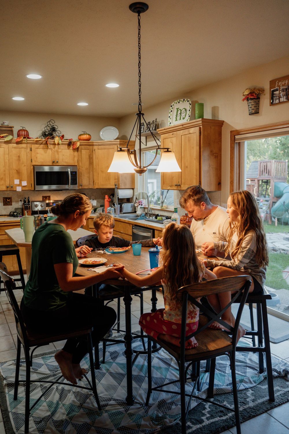 Family gathered around dining table under pendant lights in modern kitchen for mealtime.