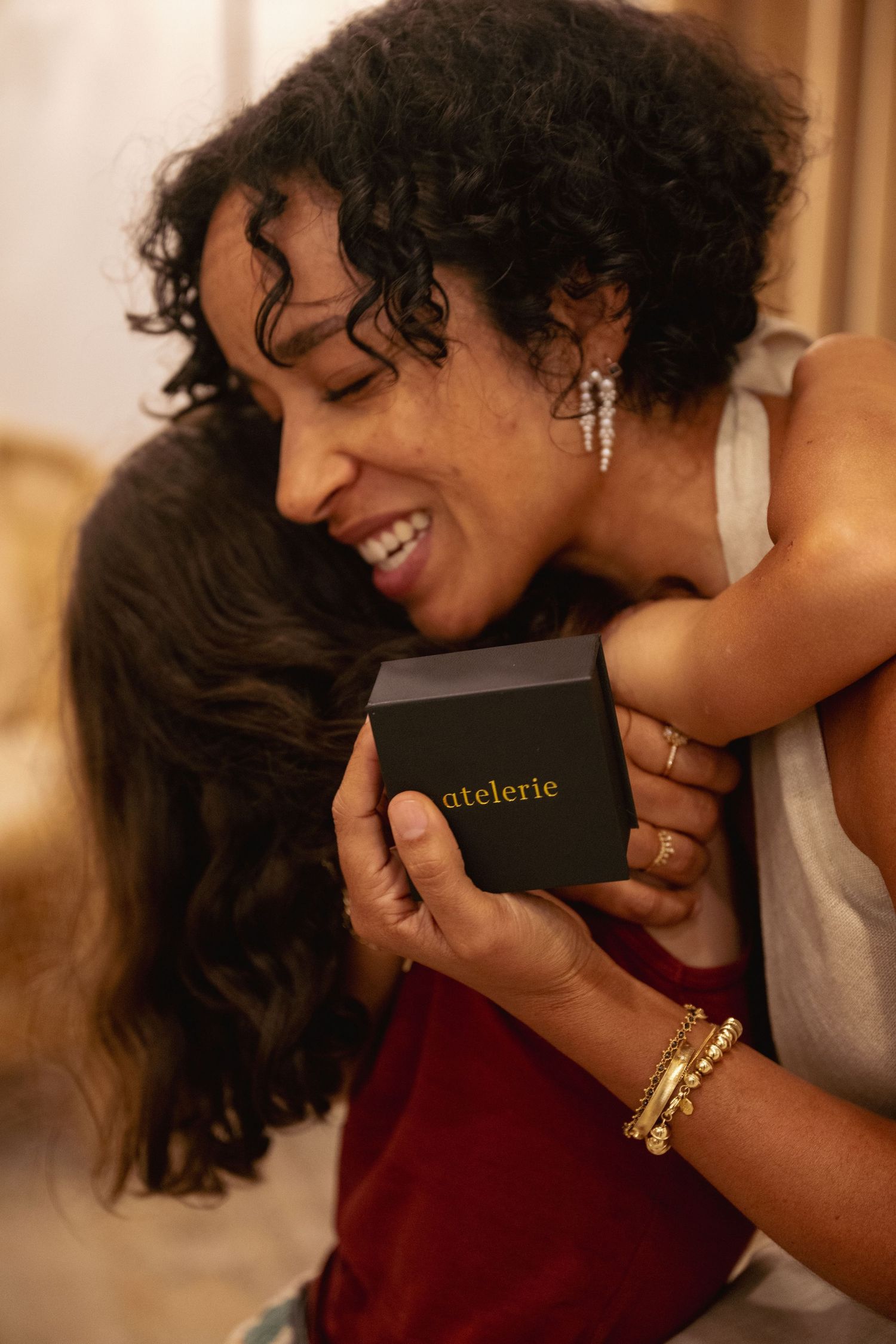 A series of warm-toned photos showing jewelry being tried on with gold bangles and rings visible against burgundy fabric.