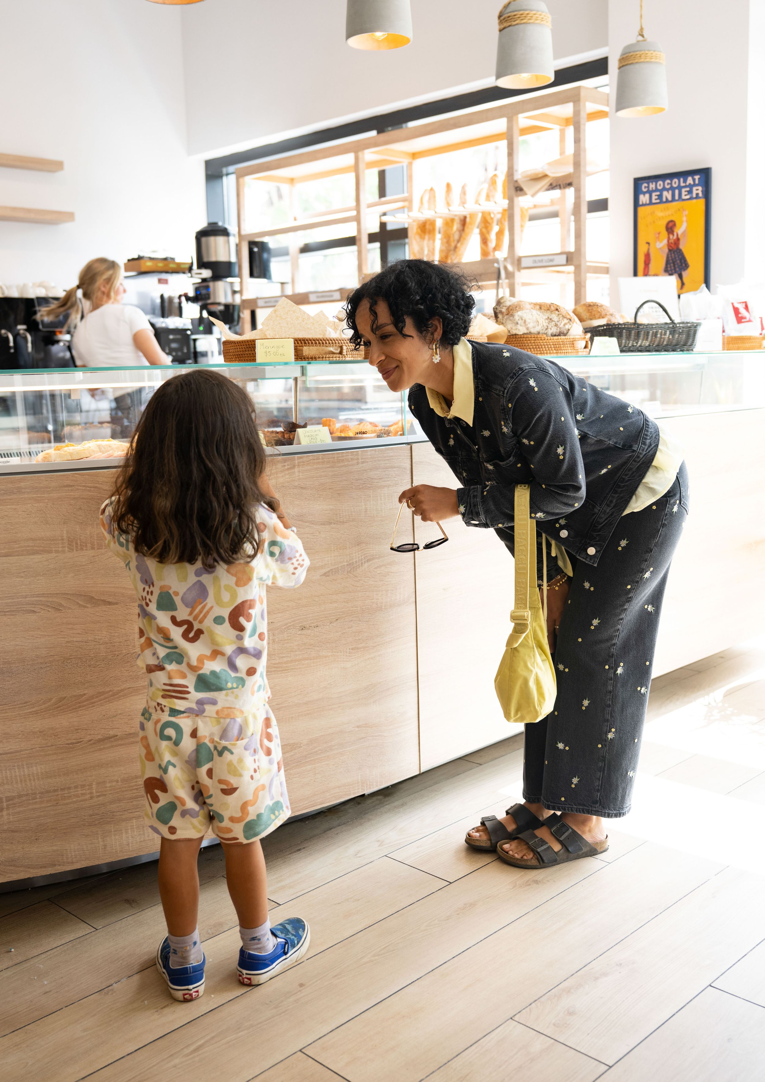 Child in colorful outfit looking at pastries displayed in a modern bakery counter.