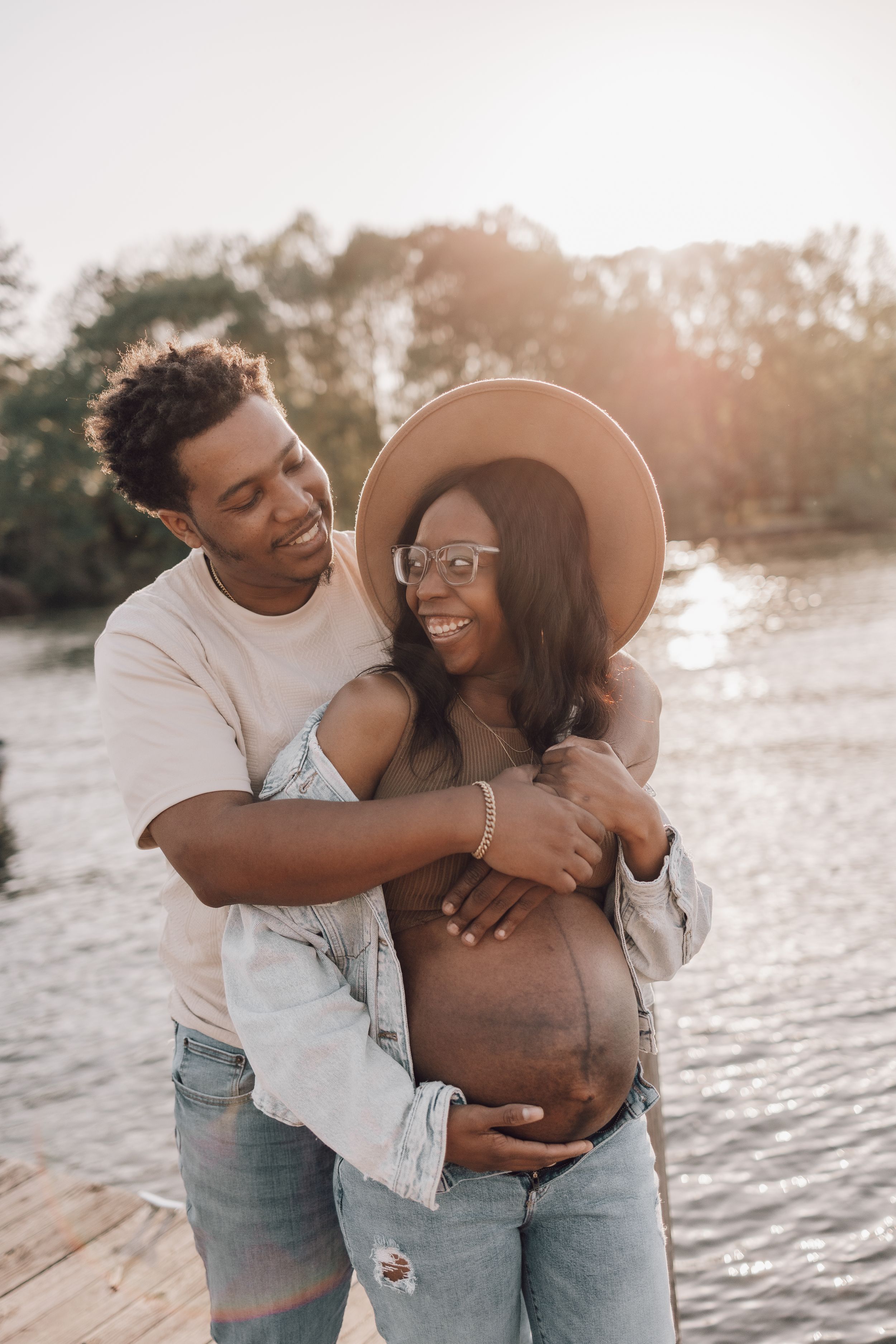 A couple shares a tender embrace on a beach at sunset wearing casual denim and white clothing.