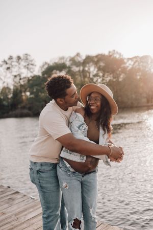 A couple shares joyful moments together on a wooden dock during sunset by the water.