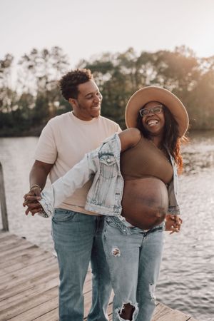 Candid beach maternity photoshoot featuring a couple in denim and white sharing joyful moments together.
