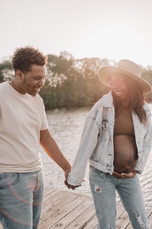 A couple in casual denim and white outfits share intimate moments while walking on a sandy beach at sunset.