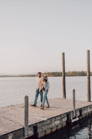 A couple sits together on a wooden dock overlooking a serene lake at sunset, creating a romantic atmosphere.