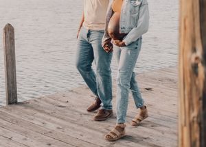 Close-up view of feet in brown leather sandals and blue jeans walking on a wooden boardwalk.
