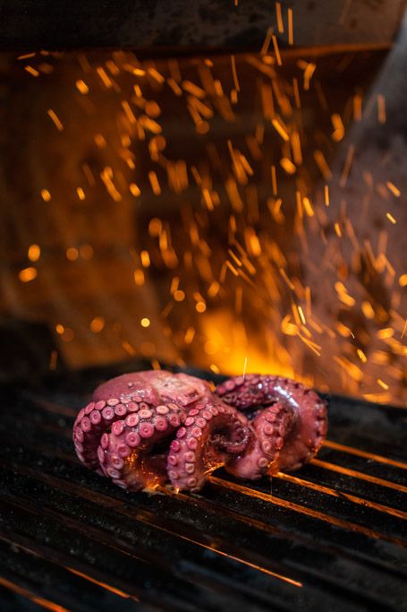 Tentáculo de pulpo a la parrilla con chispas de fuego en cocina profesional