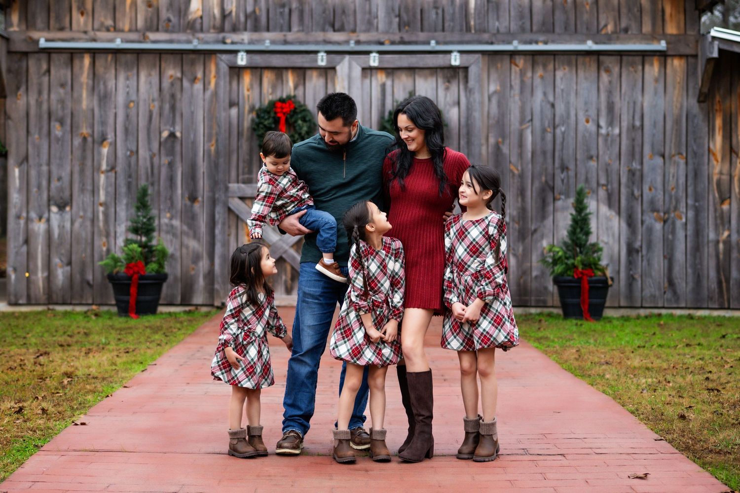 Family standing in front of a Christmas decorated barn interacting with each other.